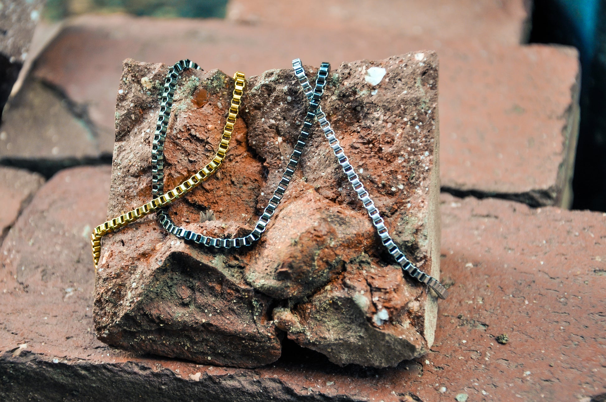 Gold, Silver and black box chain bracelets on brick