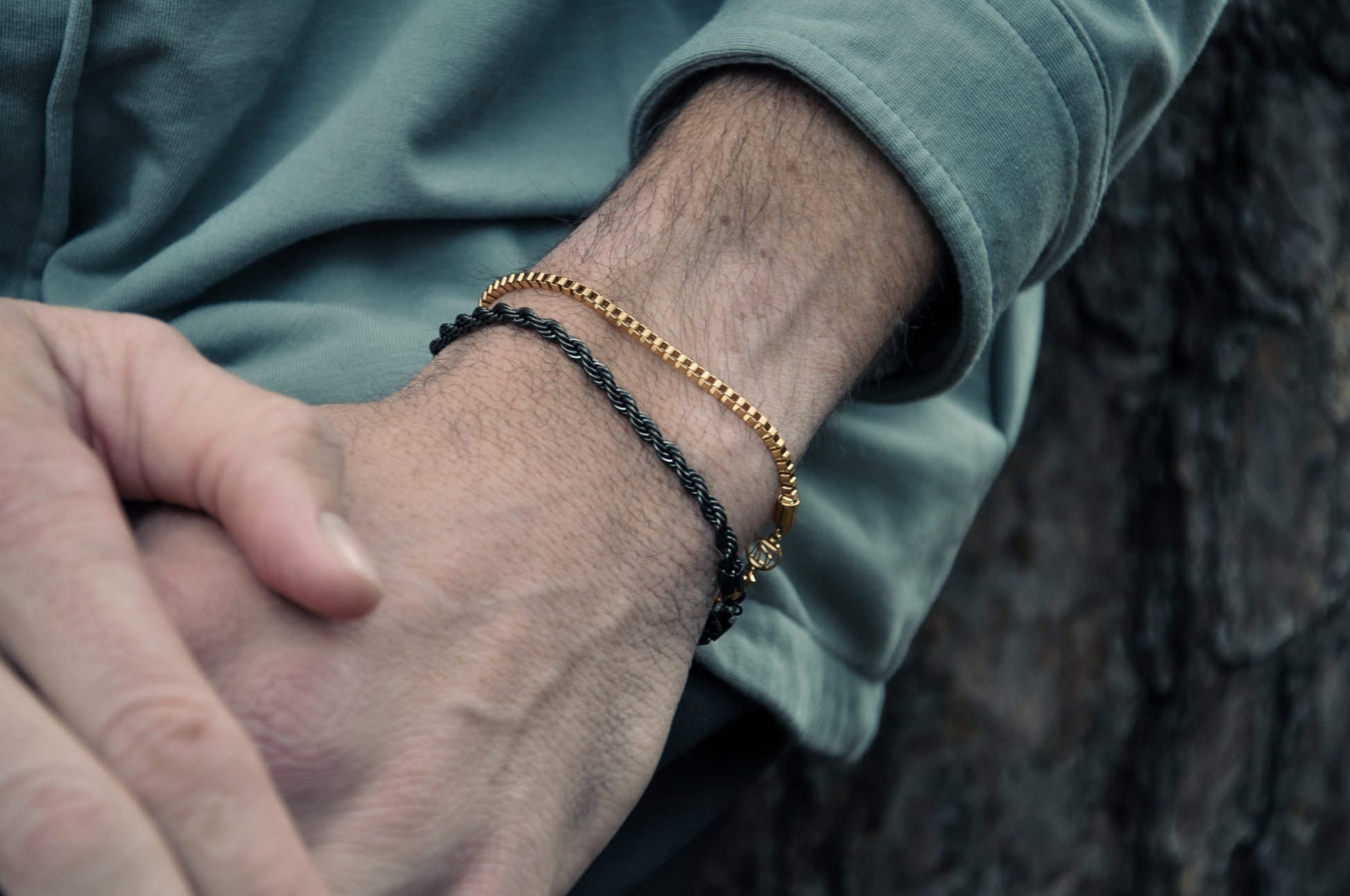 Mens wrist with black rope chain and gold box chain bracelet