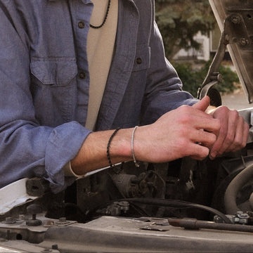 Man working on a car engine with the hood open wearing a silver box chain bracelet 