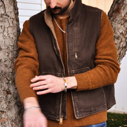Man wearing a brown jacket and vest standing next to a treen wearing jewelry